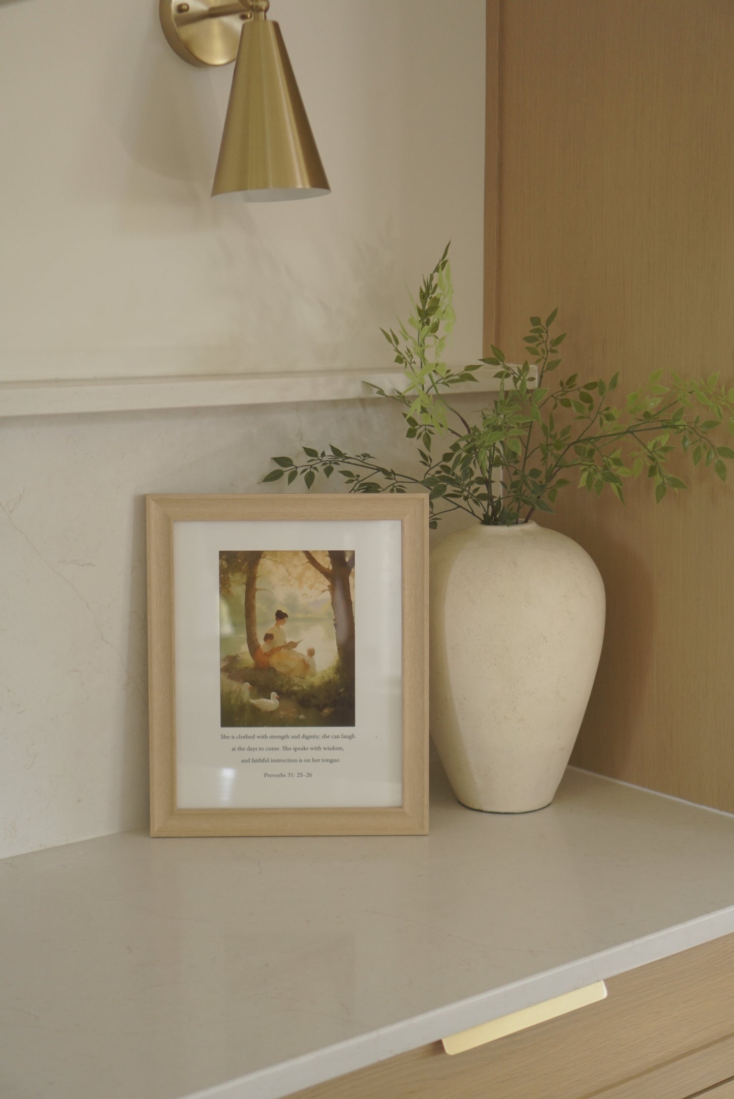 Framed picture on a wall next to a plant and light fixture. By the Pond Christian wall art modern by Christian artist capturing peace in God’s presence.