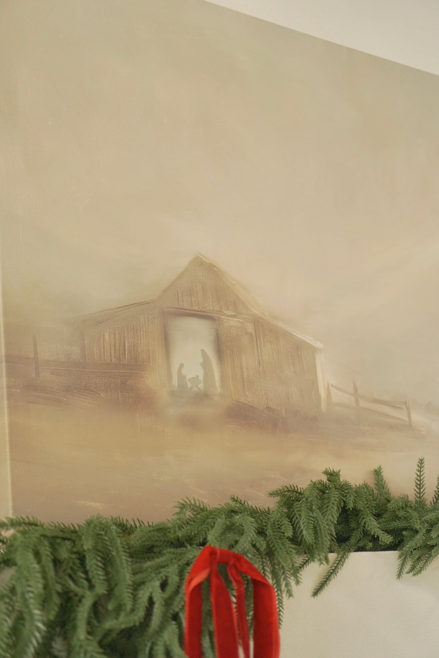 Framed print of a misty landscape with a wooden cabin on a wall above a mantel with greenery and a red ribbon. Christian Christmas artwork made by a christian artist. Nativity scene artwork.