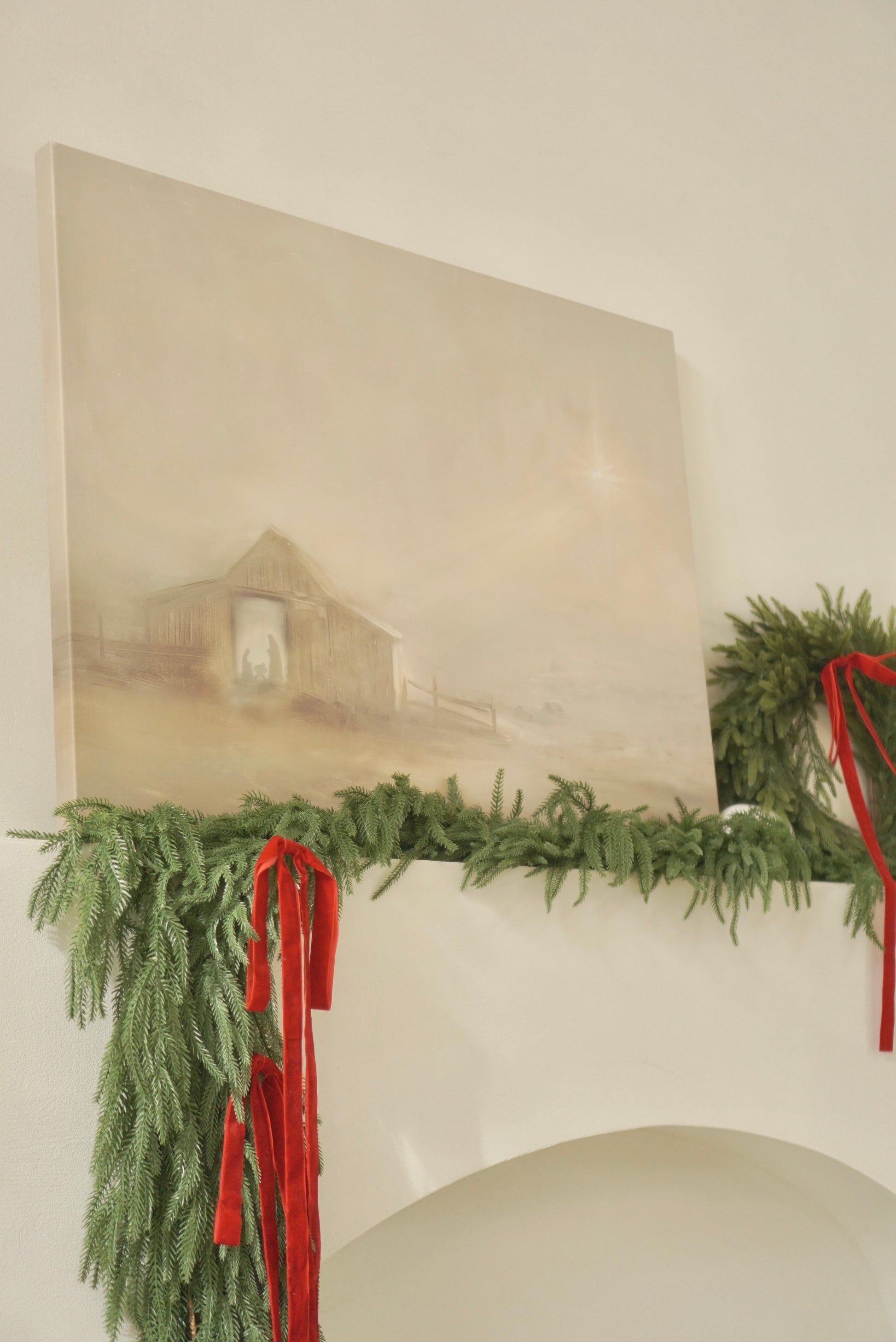Decorative mantel with greenery and red ribbons against a neutral wall with a painting. Christian Christmas artwork made by a christian artist. Nativity scene artwork.
