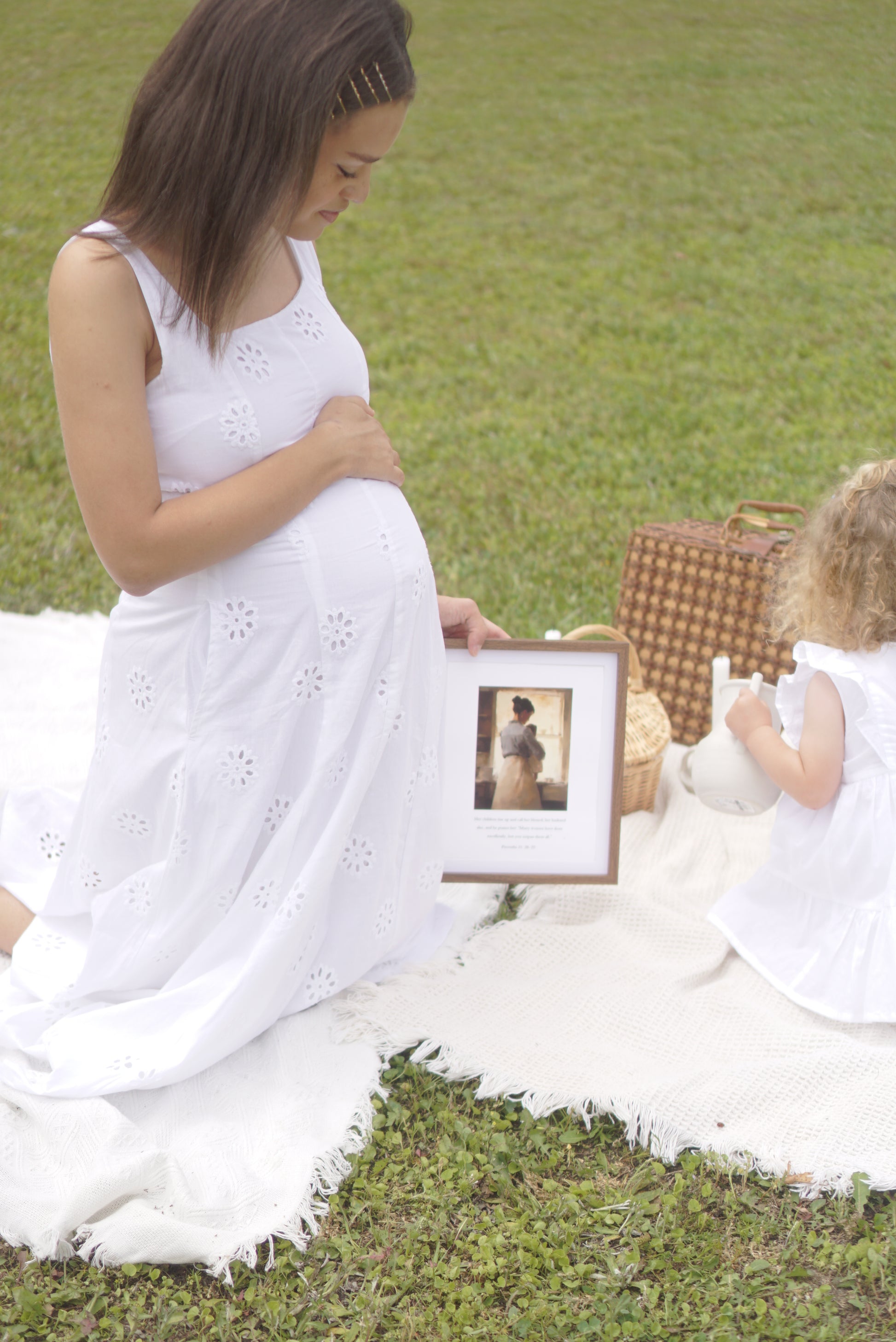 Woman in a white dress holding a framed photo of a baby, standing on grass. Proverbs 31 Scripture Print Christian wall art modern, faith-filled verse for home decor.
