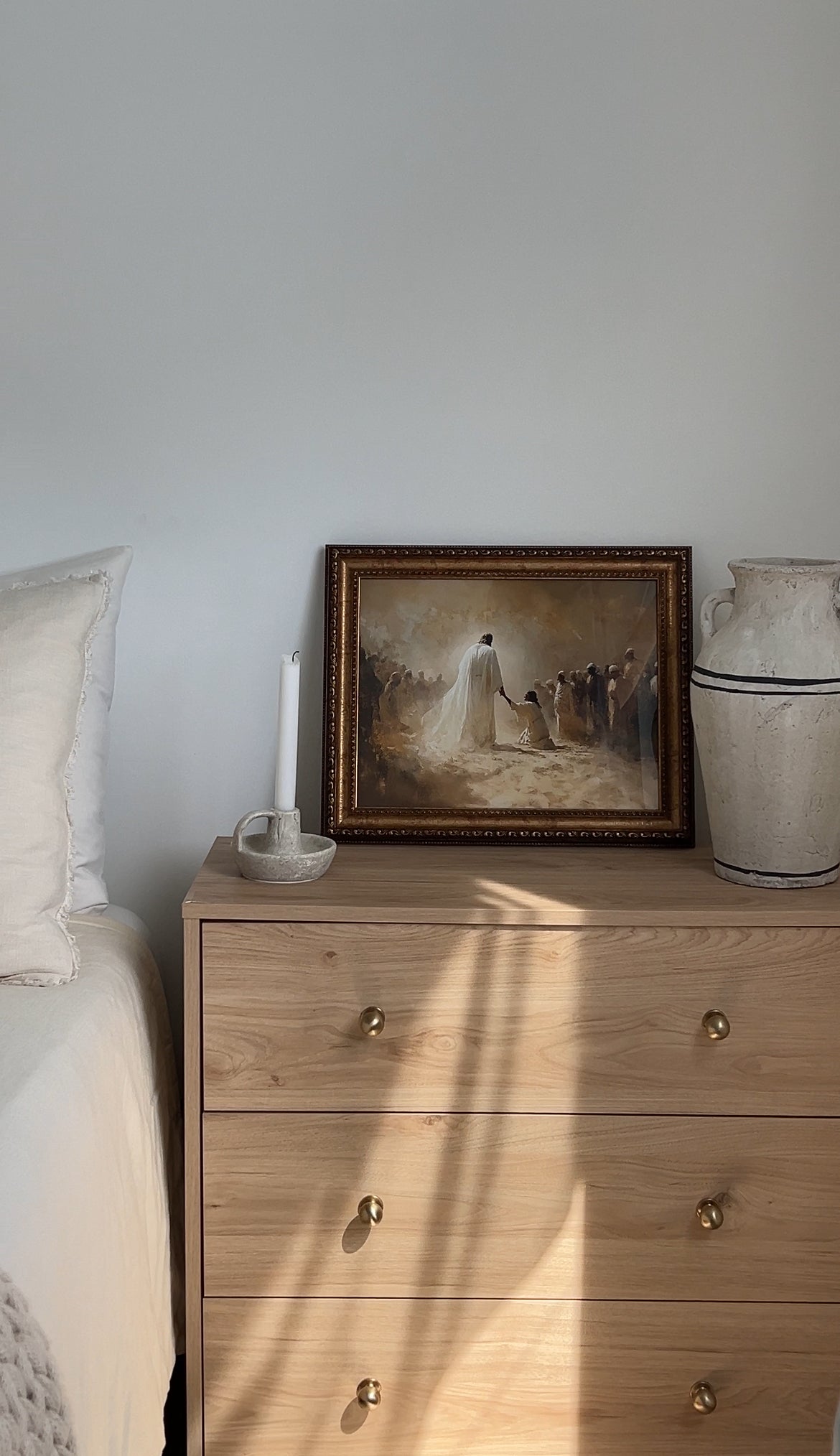 Just One Touch Print modern Christian wall art of Jesus’ healing power, faith-filled art. Wooden dresser with a framed painting and decorative vase against a white wall.